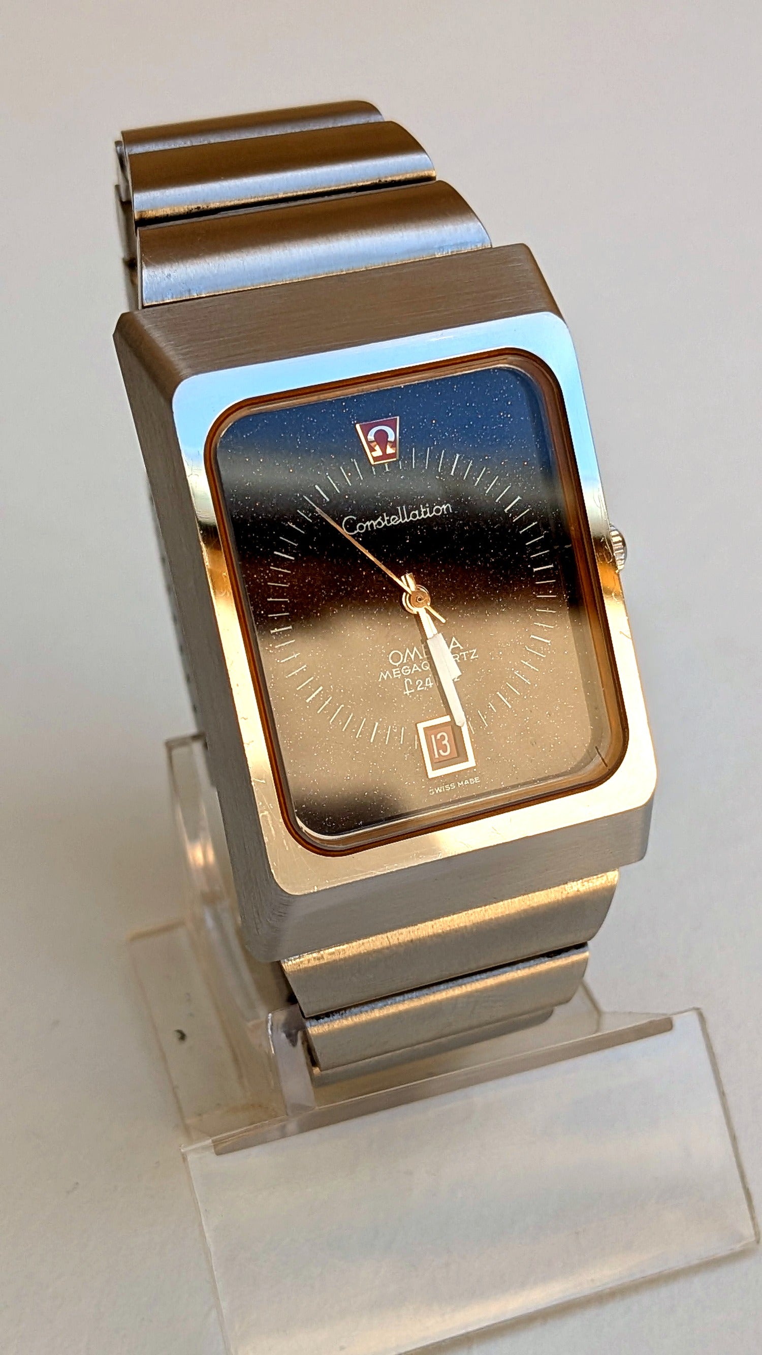 Omega Constellation Megaquartz cadran aventurine et reflets dorés sur support, guichet date, montre vintage homme